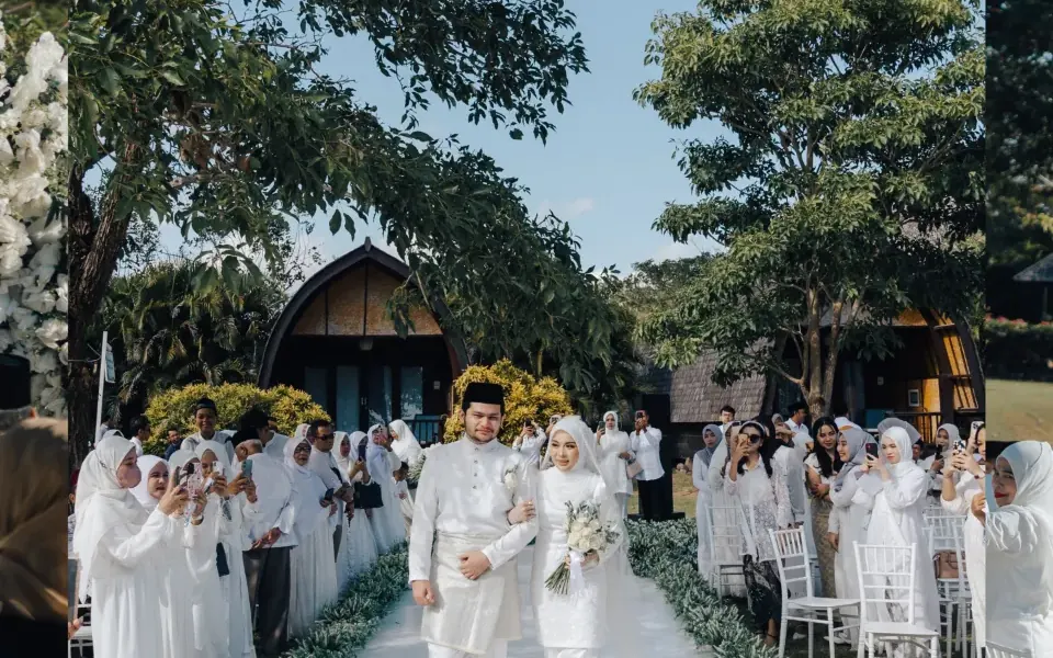 A bride and groom walking down a garden aisle between guests in white